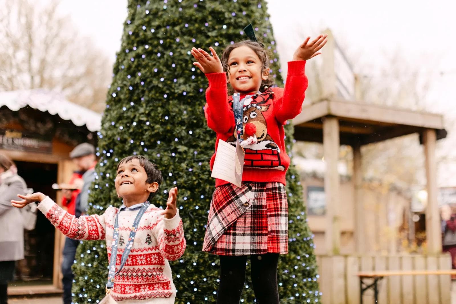Two children reaching up with joy in front of the giant illuminated Christmas tree at Christmas at Bewl Water