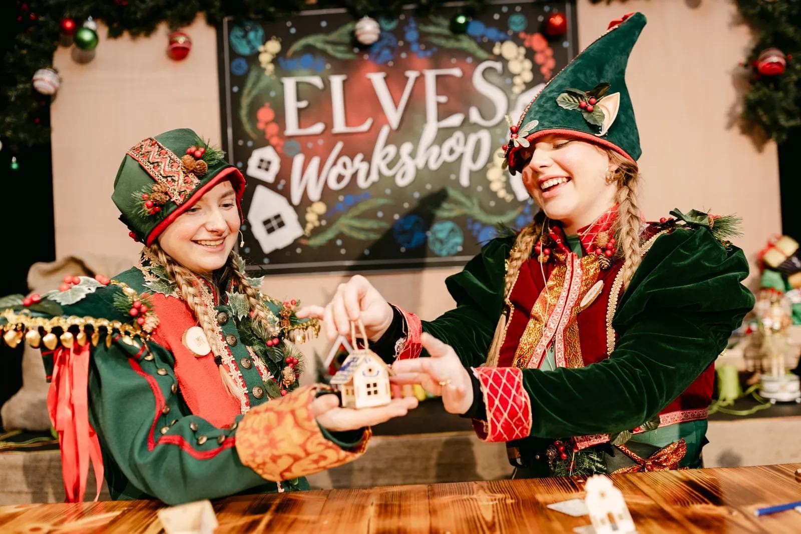 Two elves holding a handmade wooden house ornament in the Elves' Workshop