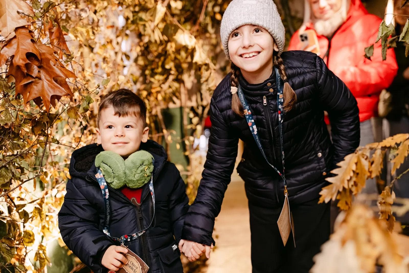 Two children walking hand in hand through a tunnel of golden leaves on the way to meet Santa