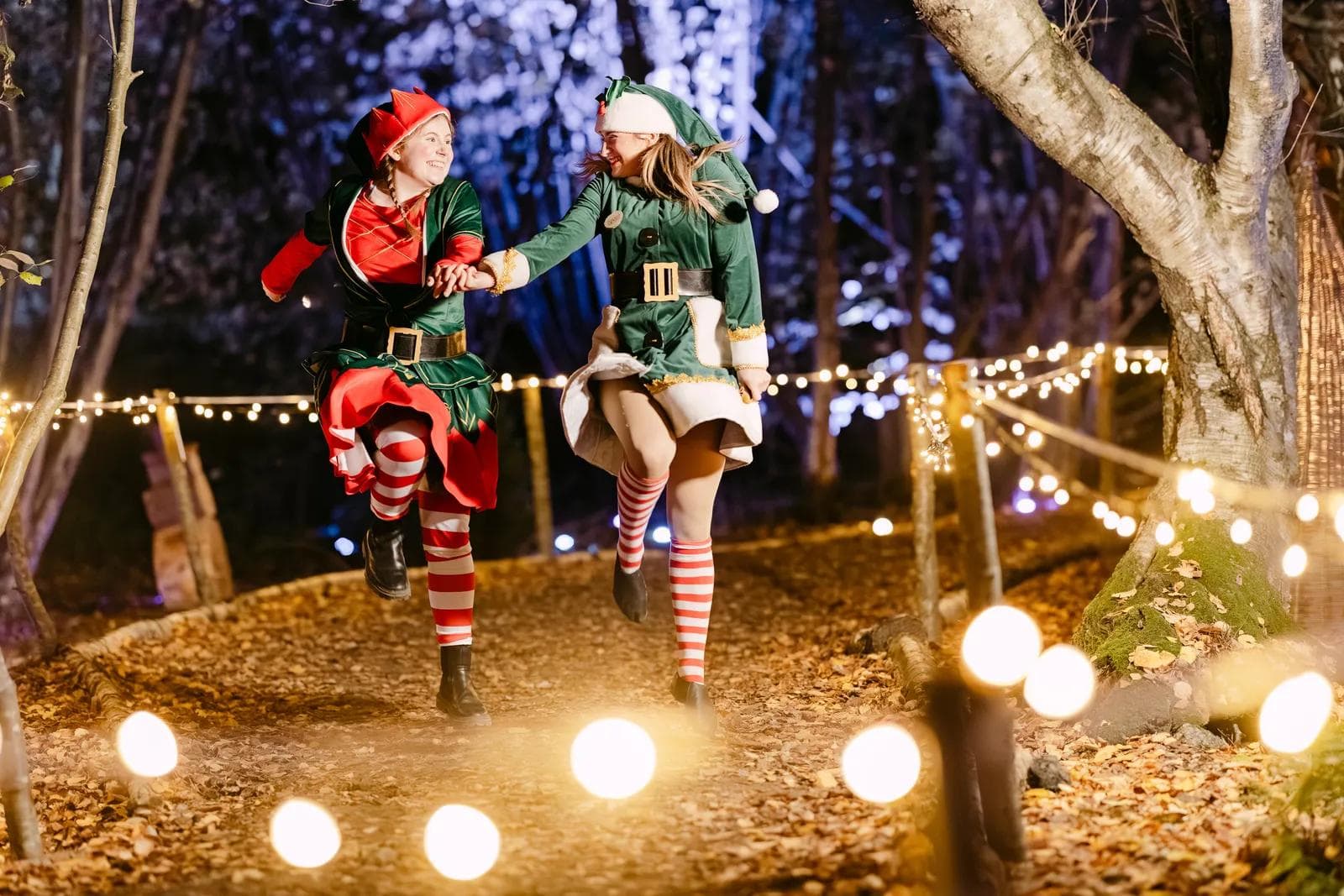 Two elves running through the fairy-lit woodland at night at Christmas at Bewl Water